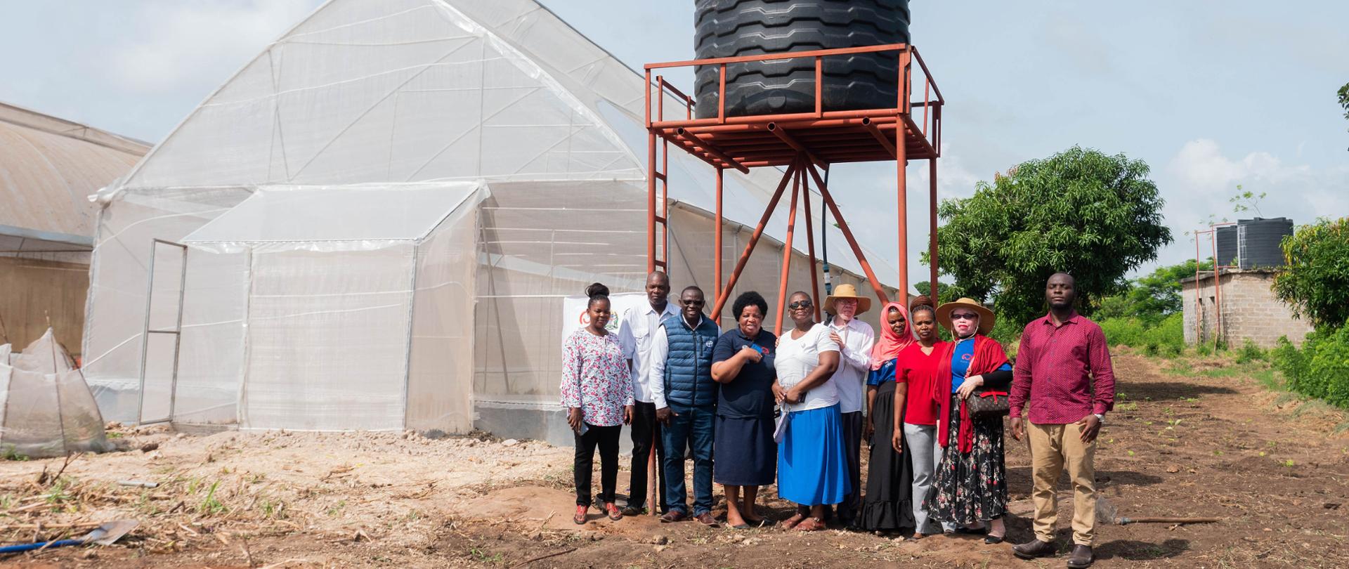 Grupa osób pozuje do zdjęcia przed zbiornikiem na wodę i szklarnią