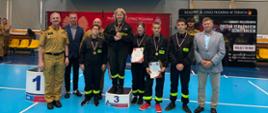 Uczestnicy II Halowych Młodzieżowych Zawodów Sportowo-Pożarniczych pozują na podium z medalami, pucharami i dyplomami po zakończonej rywalizacji.