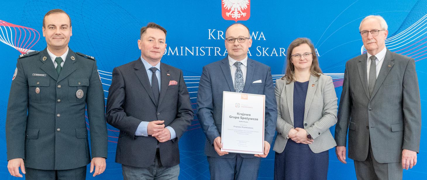 Szef KAS Bartosz Zbaraszczuk i min. Anna Chałupa pozują do zdjęcia razem z przedstawicielami firmy Krajowa Grupa Spożywcza SA.