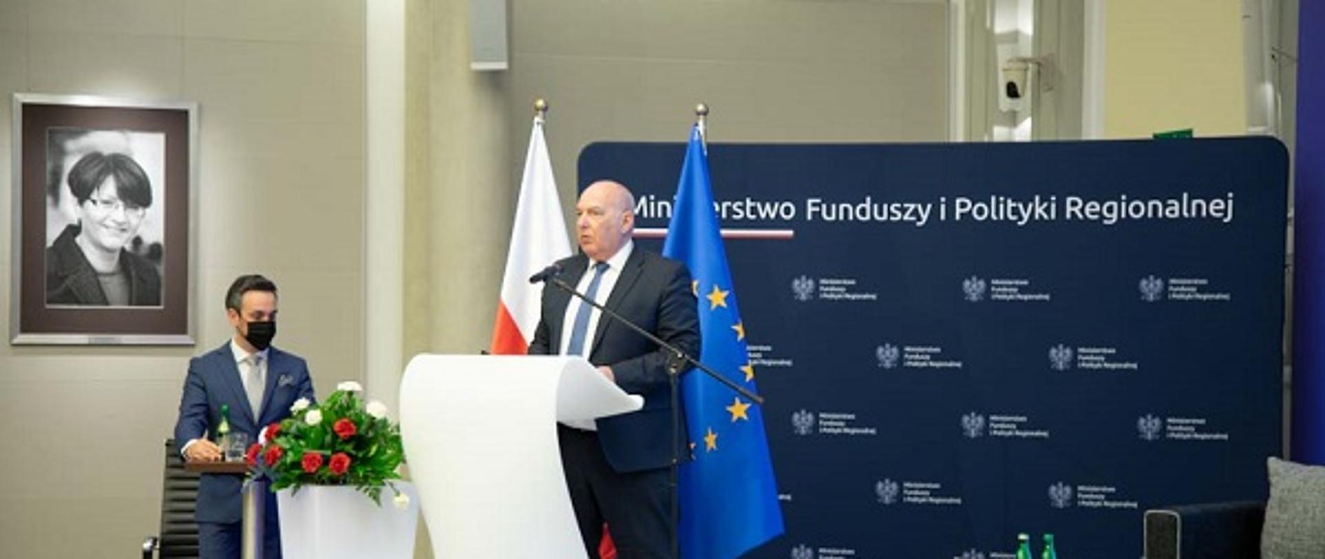 Minister Tadeusz Kościński przemawia na scenie. W tle ścianka z logo Ministerstwa Funduszy i Polityki Regionalnej
