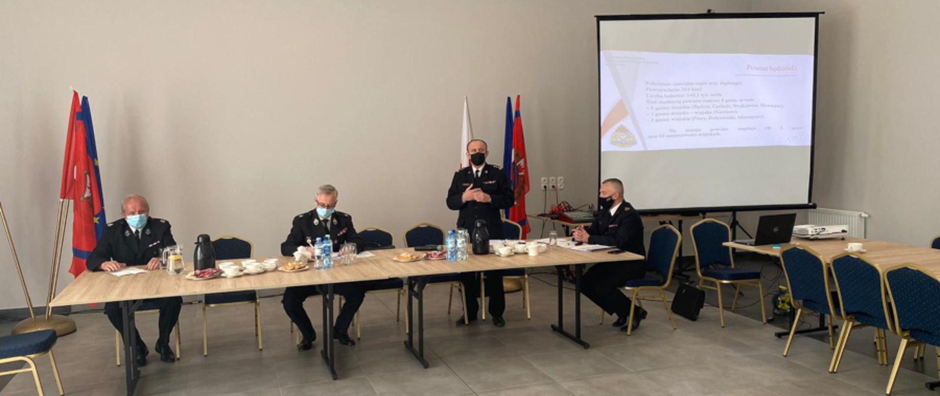 Zdjęcie wykonano wewnątrz budynku remizy Ochotniczej Straży Pożarnej podczas konsultacji projektu ustawy o ochotniczej straży pożarnej na tle jasnej ściany. Zdjęcie przedstawia st. bryg. Bogdan Jędrocha – Zastępca Śląskiego Komendanta Wojewódzkiego,mł. bryg. Arkadiusz Spera – Komendant Powiatowy PSP w Będzinie, dh Zdzisław Banaś – Wicerezes Zarządu Oddziału Wojewódzkiego Związku OSP RP Województwa Śląskiego oraz jednego z dh OSP (wszystkie osoby ubrane są w mundury służbowe)