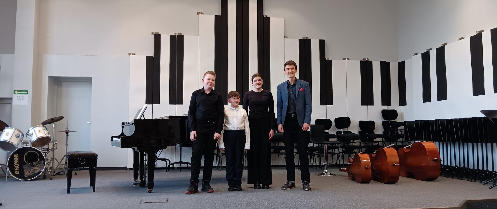 Dwóch chłopców i dziewczyna stoją z nauczycielem na scenie.