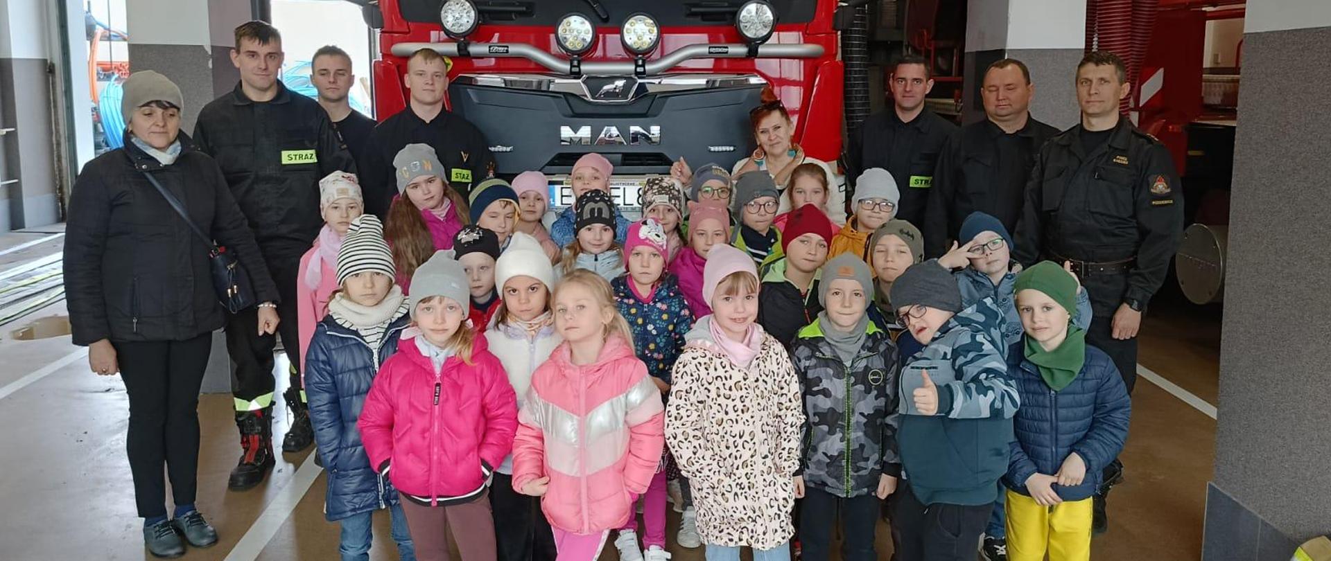 zdjęcie grupowe dzieci, dwóch opiekunek i sześciu strażaków na tle wozu strażackiego 