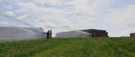 Na zdjęciu widoczne są stogi słomy oraz strażacy ćwiczący gaszenie tych stogów.