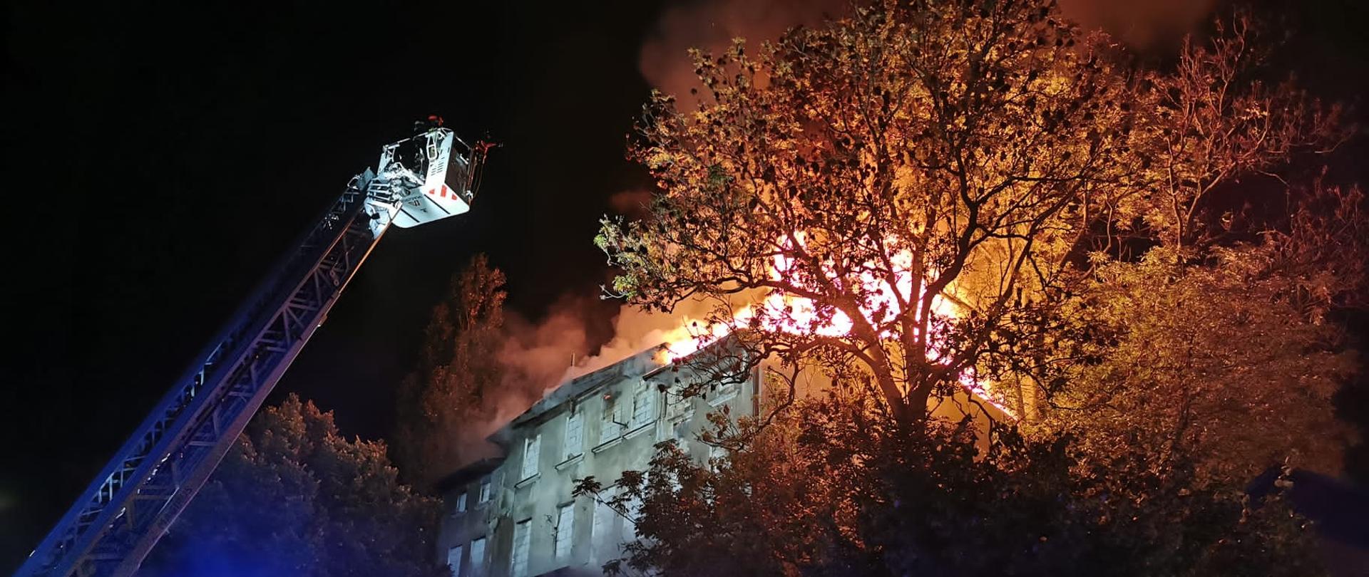 Widoczny pożar dachu pustostanu oraz drabina pożarnicza z koszem.