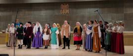 Grupa słuchaczy Studium stojąca w przebraniach z prastarej epoki na scenie Auli UAM w Kaliszu.