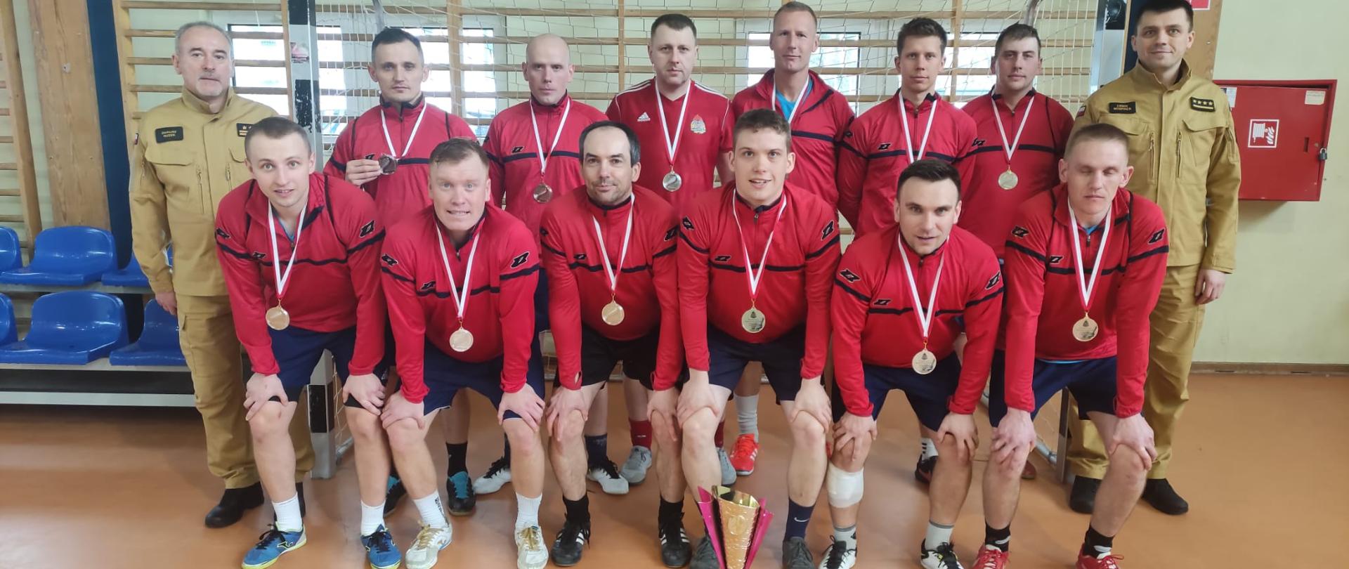 Zdjęcie grupowe wszystkich zawodników komendy państwowej straży pożarnej w brzezinach, komendanta oraz dowódcy jrg brzeziny, zdjęcie na hali na tle bramki wraz z pucharem za drugie miejsce