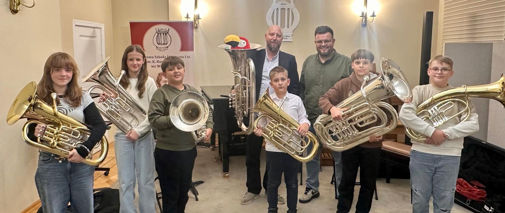 Uczniowie i pedagodzy trzymający instrumenty muzyczne.