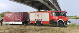 Wóz strażacki z JRG 1 Tarnów wraz z przyczepą pod mostem nad Dunajcem. Strażacy przygotowują sprzęt do ćwiczeń z ratownictwa chemiczno-ekologicznego.
