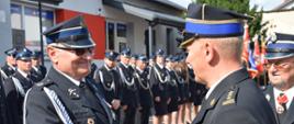 strażacy ochotnicy w mundurach galowych w czasie uroczystości, starszy brygadier Zbigniew Łyszkowicz gratuluje jednemu z druhów