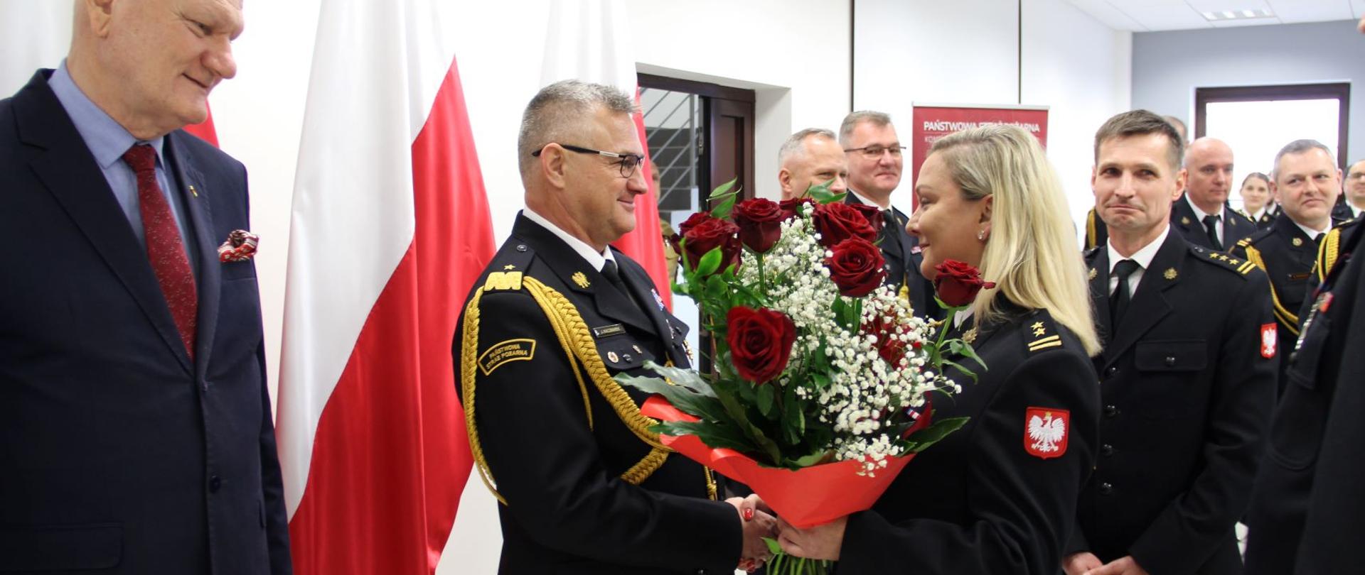 Komendant odbiera kwiaty od załogi. W tle flagi narodowe i goście.