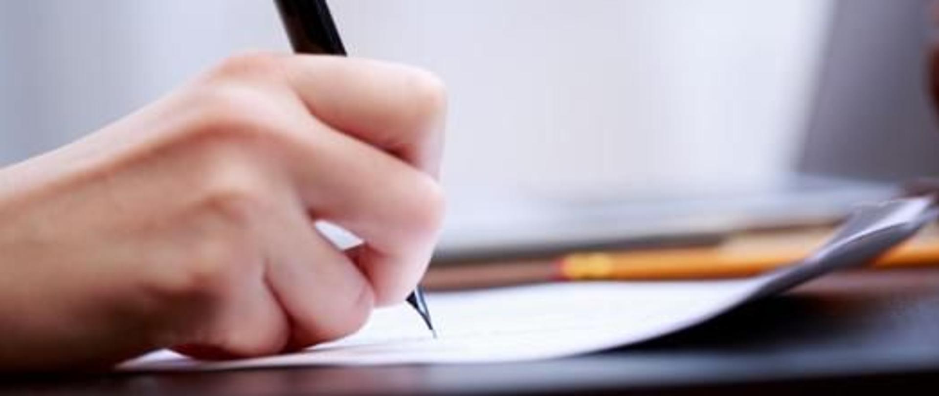 zdjęcie dłoni trzymającej pióro nad kartką
