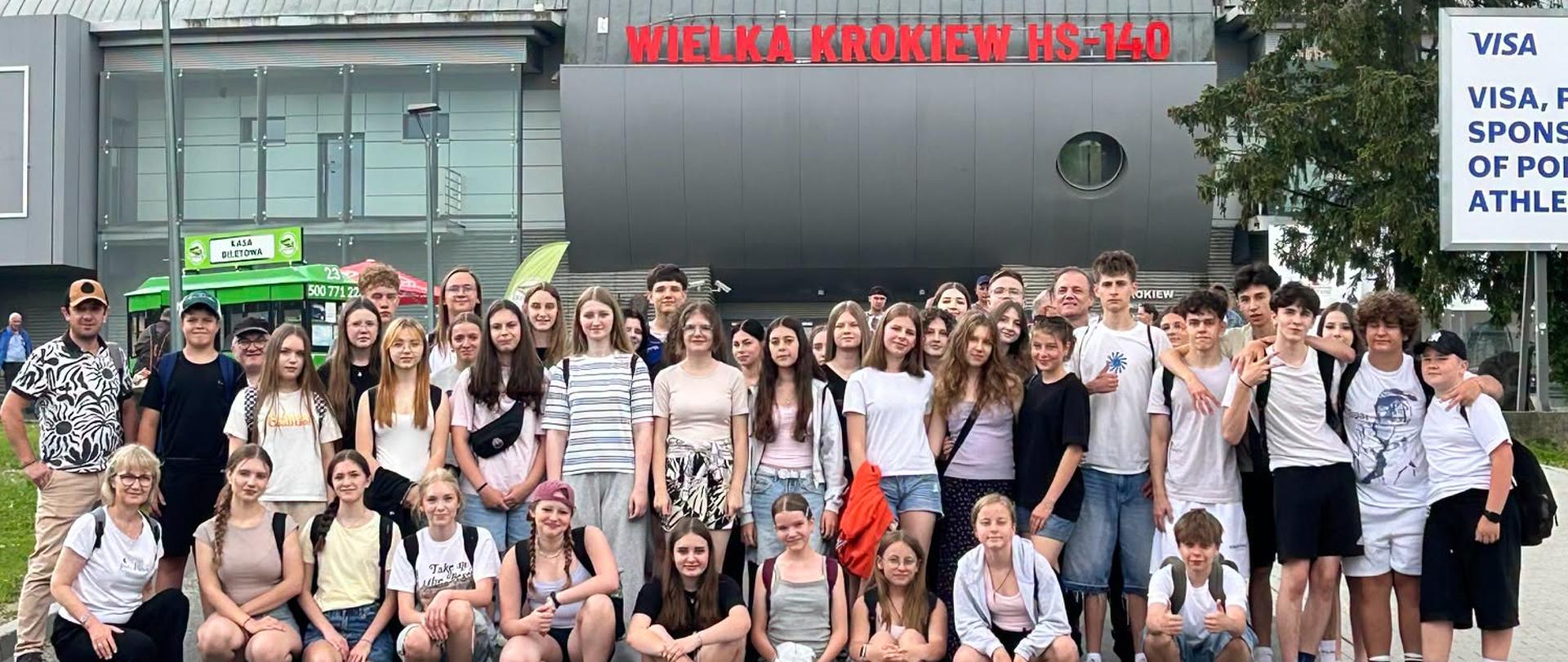 Duża grupa uczniów i opiekunów pozuje do zdjęcia przed skocznią narciarską Wielka Krokiew HS-140 w Zakopanem podczas wycieczki rekreacyjnej.