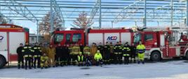 Zdjęcie przedstawia strażaków uczestniczących w warsztatach oraz pracowników firmy AirLiquide Polska Sp. z o.o. na tle samochodów strażackich.