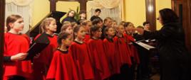 Zdjęcie kolorowe. Uczniowie i nauczyciele Państwowej Szkoły Muzycznej - chór szkolny. Grupa śpiewających dzieci w strojach czerwonych. Z prawej strony dyrygentka Liliana Zdolińska.