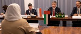 Minister Nowak siedzi za stołem z członkami polskiej delegacji. Zwraca się do ambasadorki. na zdjęciu widać jej plecy.