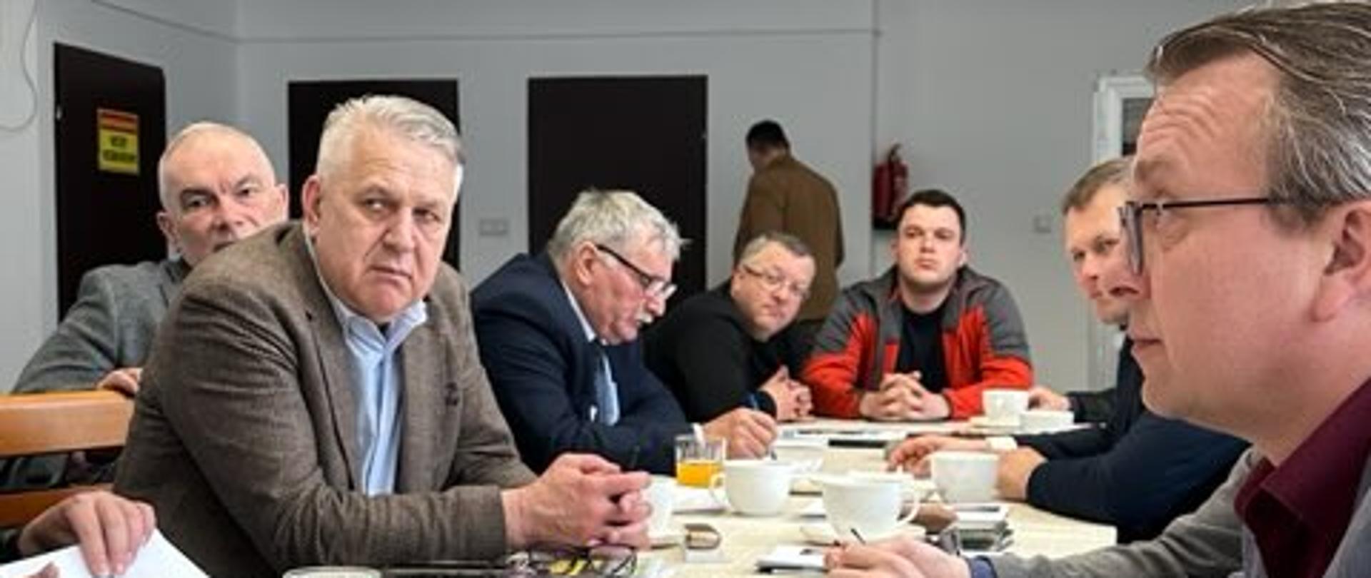 Mężczyźni przy stole, każdy z filiżanką kawy, prowadzący ożywioną dyskusję.