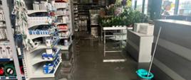 Usuwanie skutków intensywnych opadów deszczu. Zdjęcie wnętrze marketu budowlanego, do którego wdarła się woda. Na regałach znajduje się towar oferowany do sprzedaży.