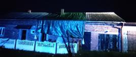 Budynek jednorodzinny zabezpieczony plandeką. Pora nocna. Oświetlenie sztuczne. Dach z eternitu.
