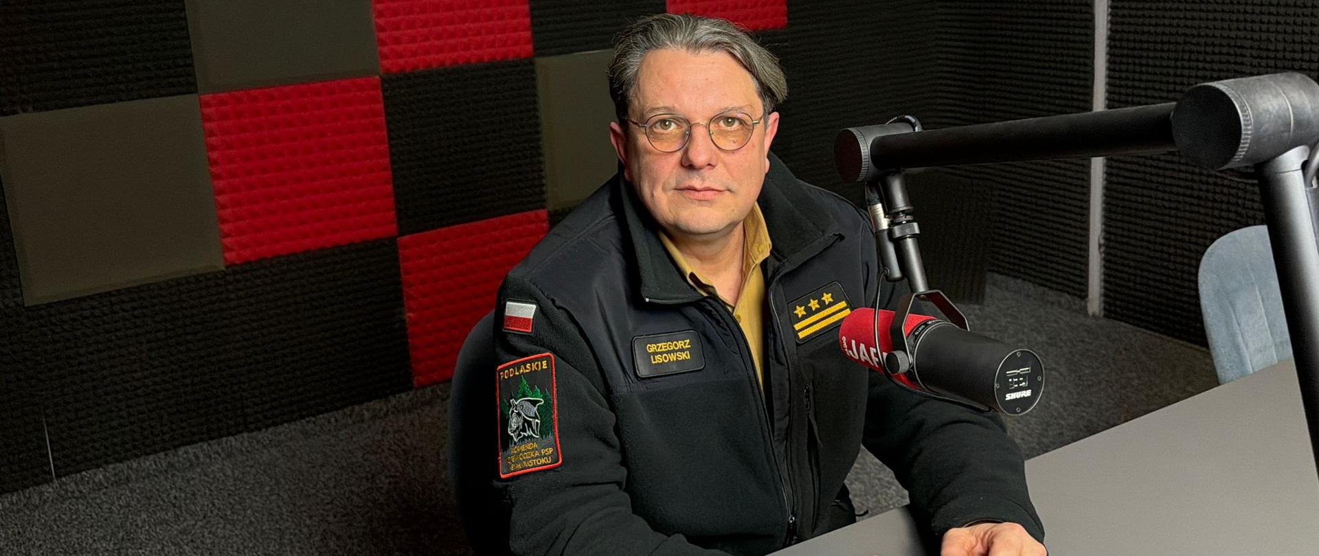 Gościem Radia Jard był zastępca podlaskiego komendanta wojewódzkiego Państwowej Straży Pożarnej, st. bryg. Grzegorz Lisowski. Strażak siedzi za mikrofonem, w tle logo radia