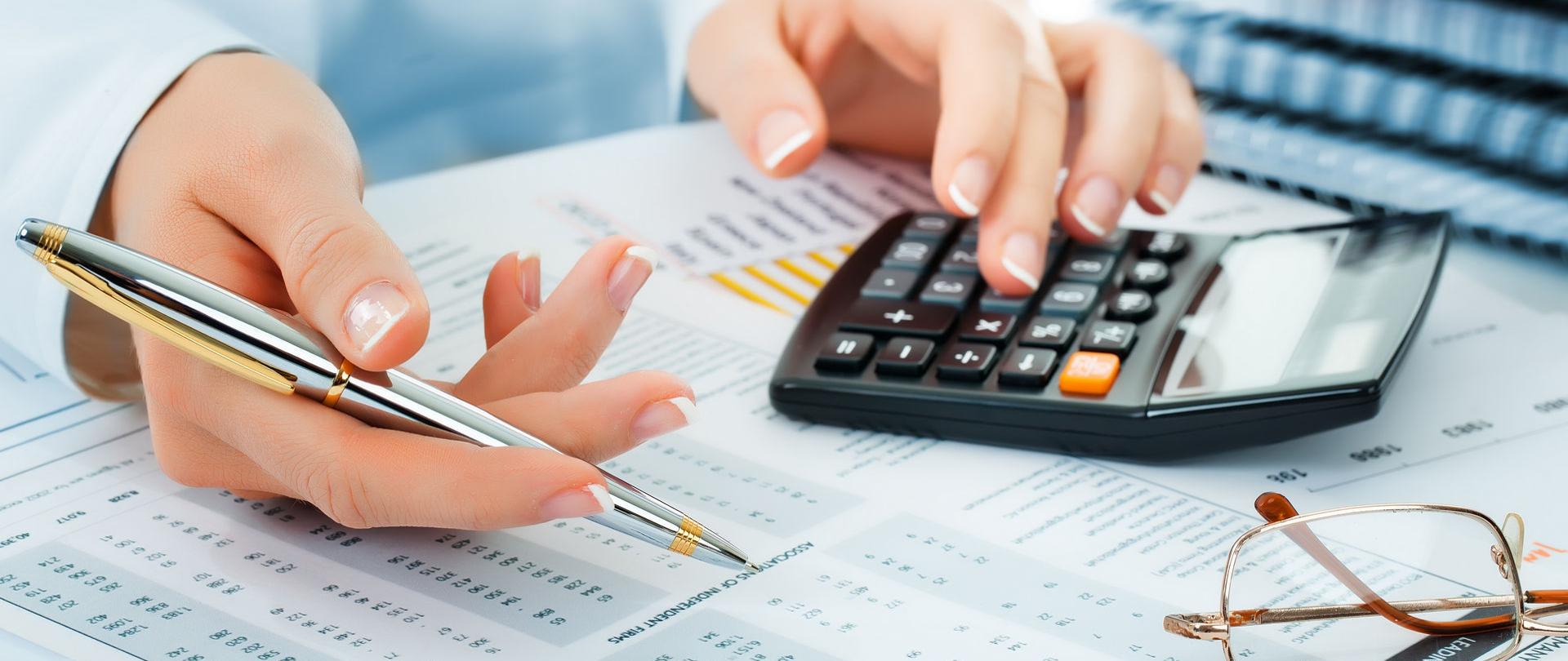 Dłonie osoby, która sprawdza dokumenty, trzyma kalkulator i długopis.