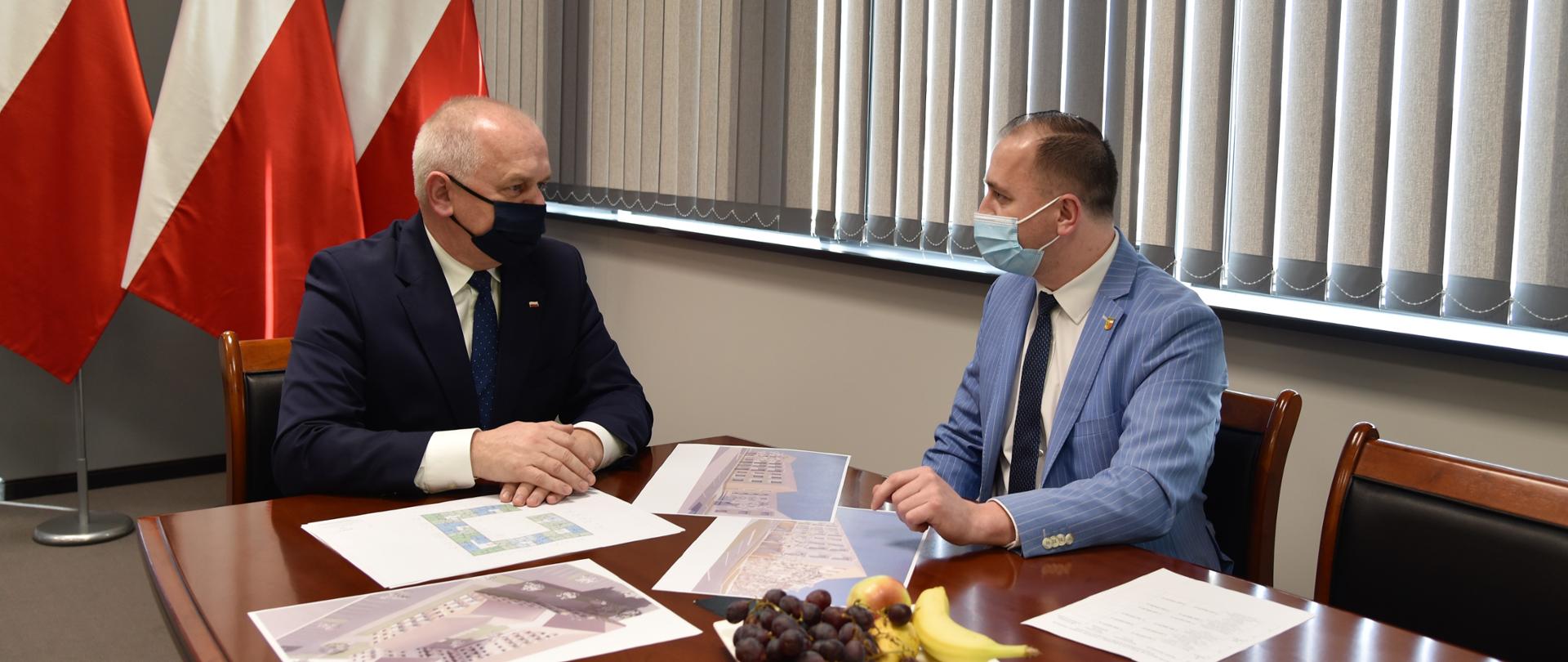 Wojewoda z burmistrzem Witnicy rozmawiają przy stole. W tle flagi.