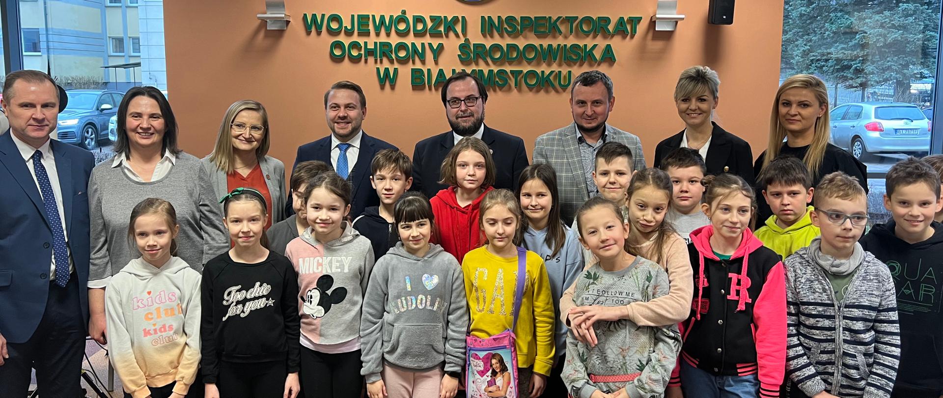 Minister Jacek Ozdoba, p.o. GIOŚ Magda Gosk, p.o. z-cy GIOŚ Krzysztof Gołębiewski oraz Podlaski WIOŚ Mirosław Michalczuk wraz z pracownikami WIOŚ w Białymstoku wraz z dziećmi pozują do zdjęcia. 