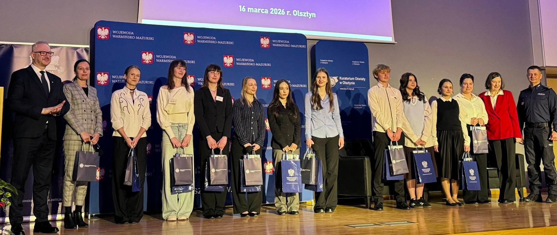 Konferencja interdyscyplinarna „Dopuśćmy dzieci i młodzież do głosu – przeciwdziałanie przemocy rówieśniczej” : na scenie organizatorzy i uczestnicy spotkania, wśród nich wojewoda Radosław Król.