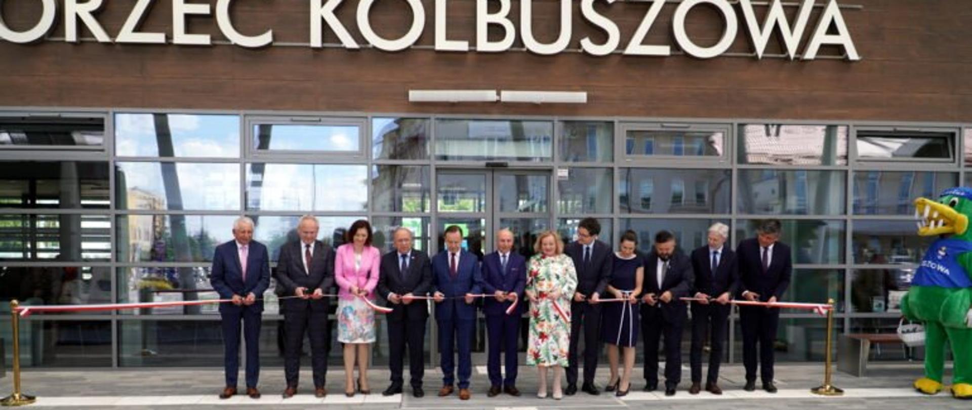 Uczestnicy uroczystości otwarcia centrum przesiadkowego w Kolbuszowej przecinają wstęgę przed budynkiem dworca