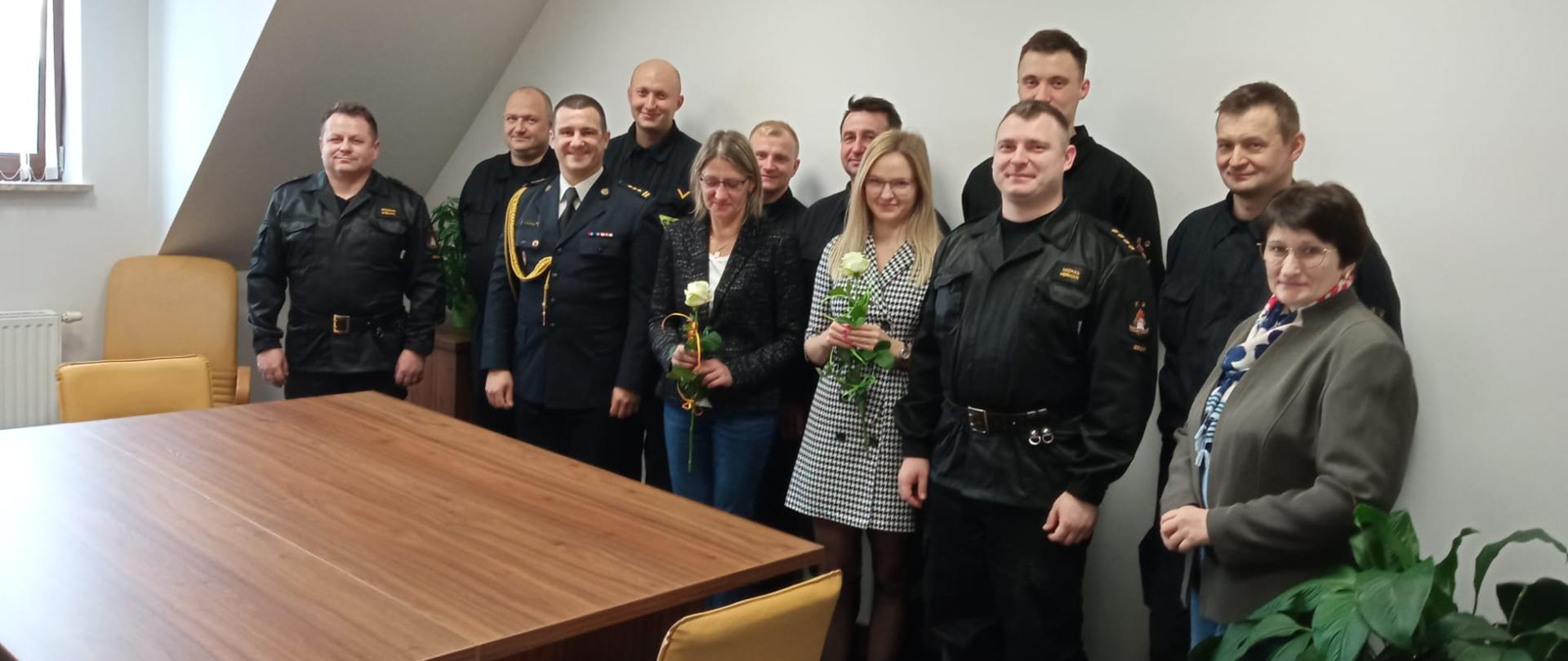 Zdjęcie przedstawia funkcjonariuszy oraz pracowników korpusu służby cywilnej Komendy Powiatowej Państwowej Straży Pożarnej w Gołdapi, które trzymają białą różę, po złożeniu życzeń i podziękowań z okazji zwyczajowo przypadającego 11 listopada Dnia Służby Cywilnej