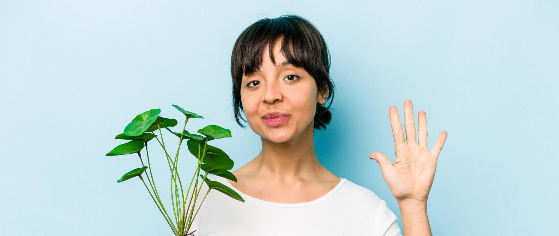 Young hispanic woman holding a plant isolated on blue background smiling cheerful showing number five with fingers.