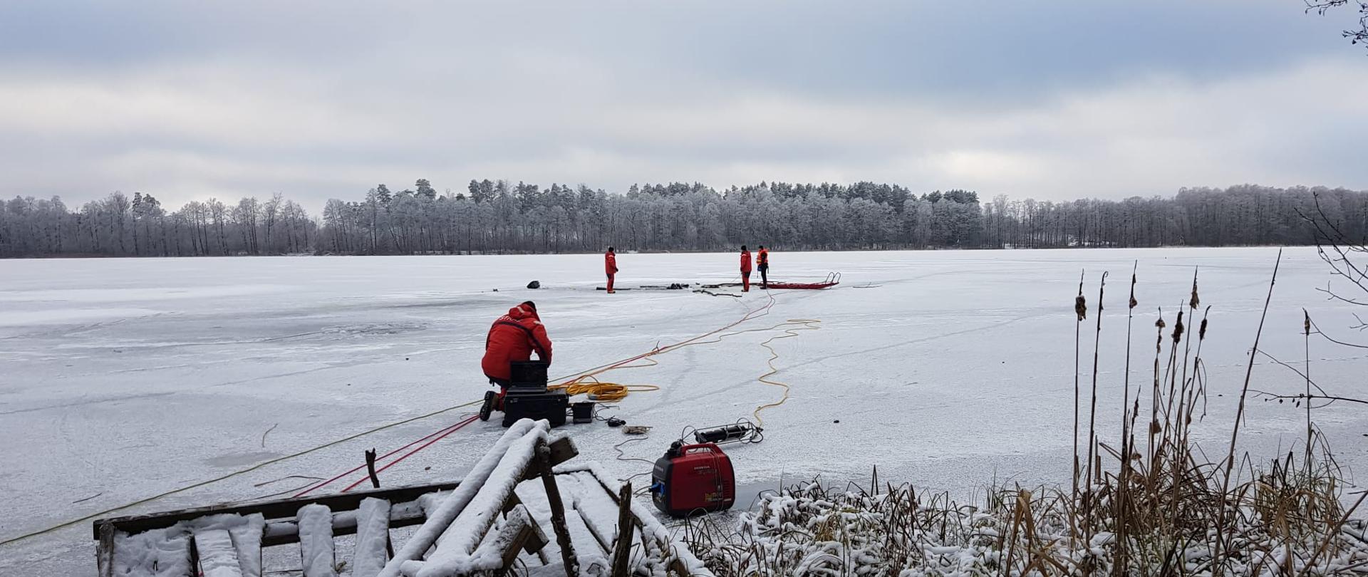 Strażacy-nurkowie na tafli lodu wspomagają pracę nurka pod wodą
