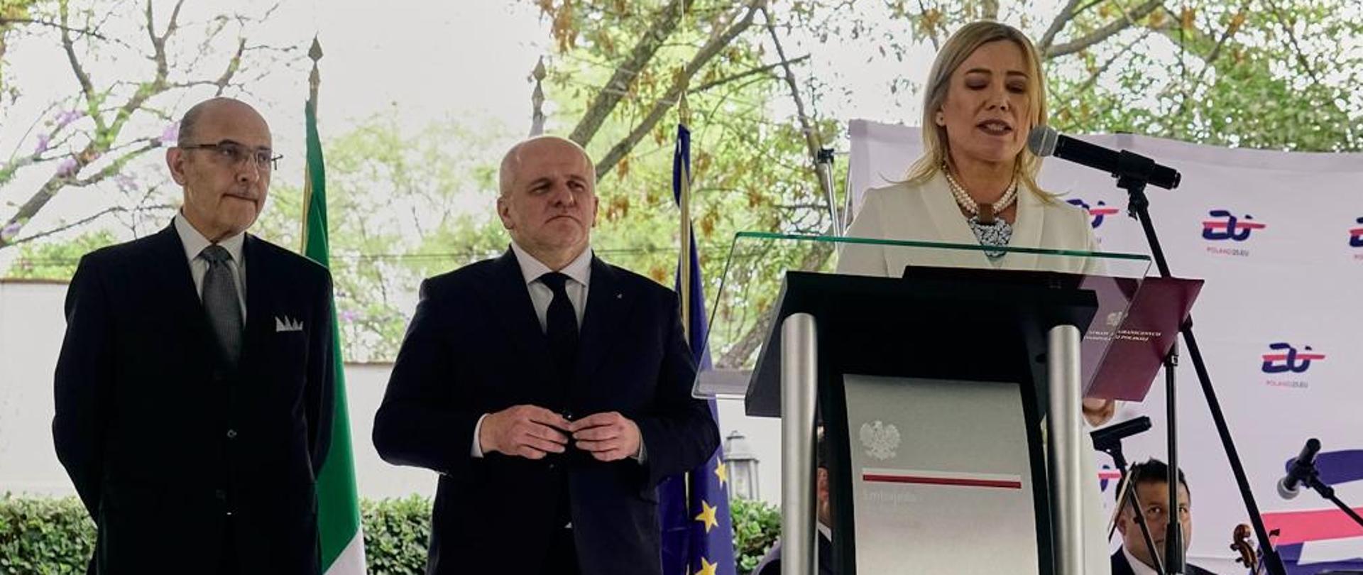 Przy mównicy w plenerze stoi Ambasador RP w Meksyku, Agnieszka Frydrychowicz-Tekieli. W tle poseł Paweł Kowal oraz Octavio Tripp Villanueva, Dyrektor Generalny ds. Europy w meksykańskim MSZ.