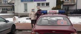 Zdjęcie przedstawia samochód ochotniczej straży pożarnej oraz osoby dowiezione do punktu szczepień.