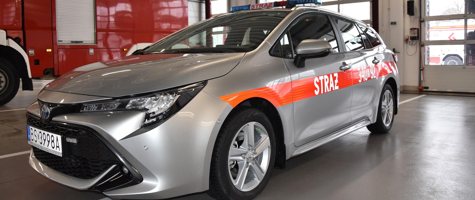 samochód operacyjny lekki o kolorze srebrnym z czerwonym pasem i napisem straż