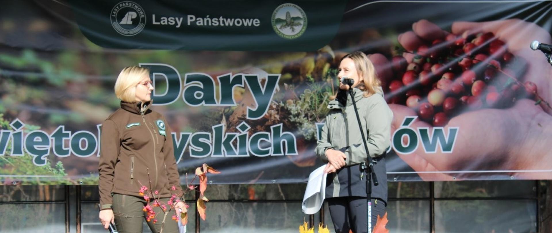 Dwie kobiety stojące na scenie, jedna mówi do mikrofonu