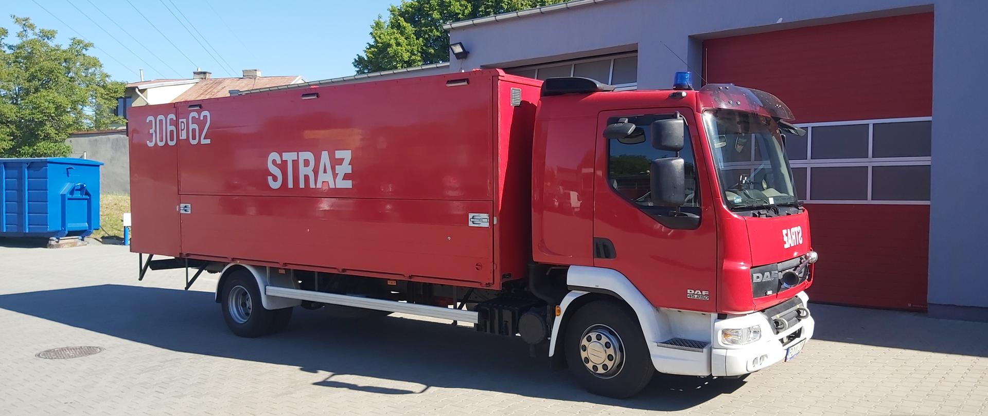 Zdjęcie przedstawia samochód ratownictwa chemicznego, który stoi na placu jednostki przed garażami. 