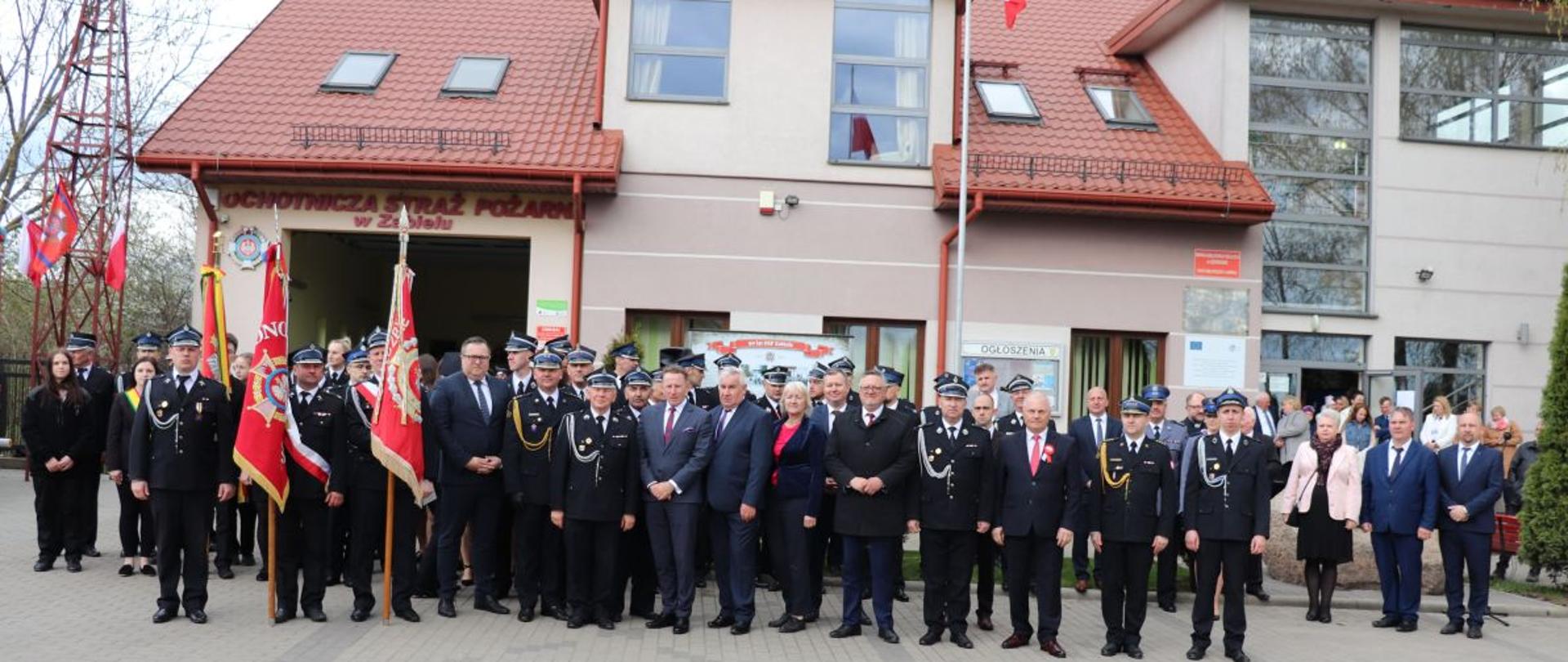 Na zdjęciu znajdują się strażacy z OSP Zabiele wraz z zaproszonymi gośćmi stojący przed strażnicą OSP.