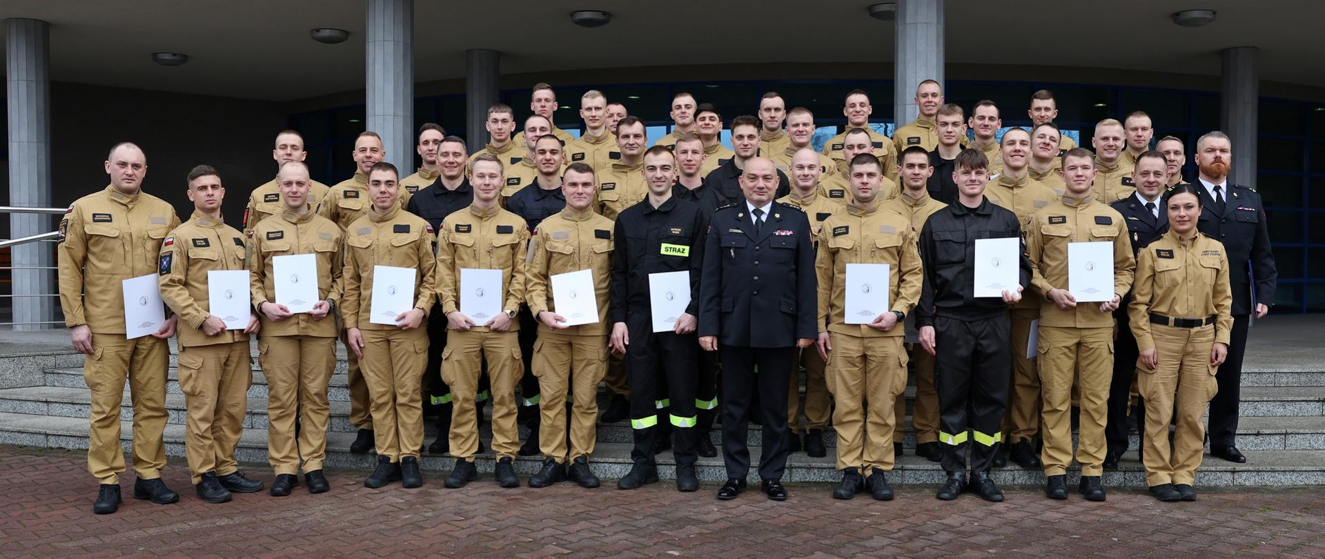 Pamiątkowe zdjęcie grupowe funkcjonariuszy PSP kończących szkolenie podstawowe (36 osób) w towarzystwie Komendanta Centralnej Szkoły, funkcjonariuszki wydziału nauczania CS PSP oraz sześciu funkcjonariuszy wydziału nauczania CS PSP