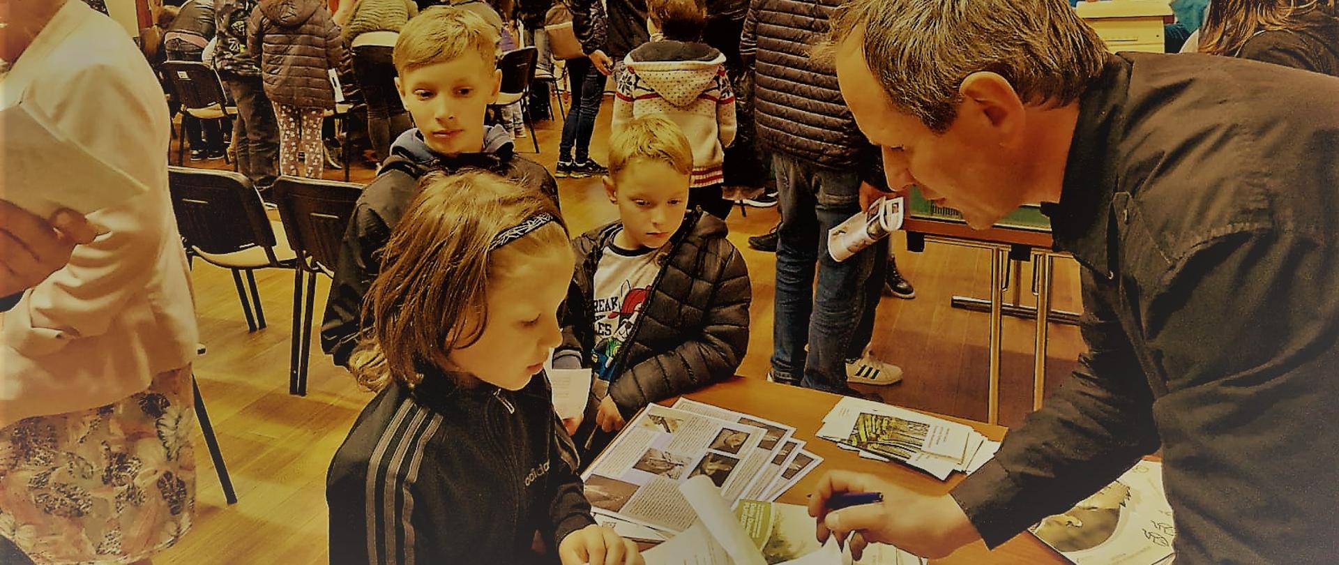 Zdjęcie dzieci zasłuchanych w słowa animatora przy stoisku RDOŚ w Krakowie 