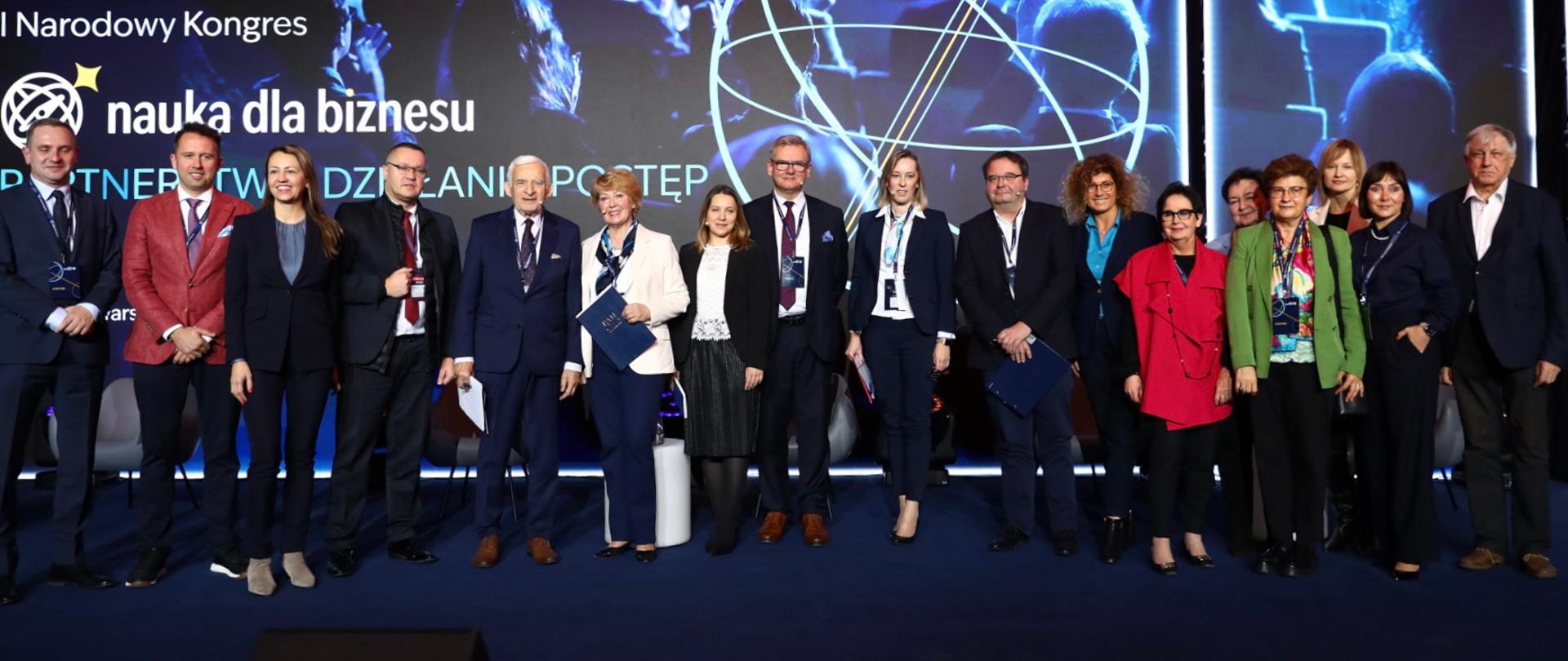 Zdjęcie zbiorowe, na tle wielkiego ekranu z napisem Nauka dla Biznesu stoi grupa kilkudziesięciu osób.