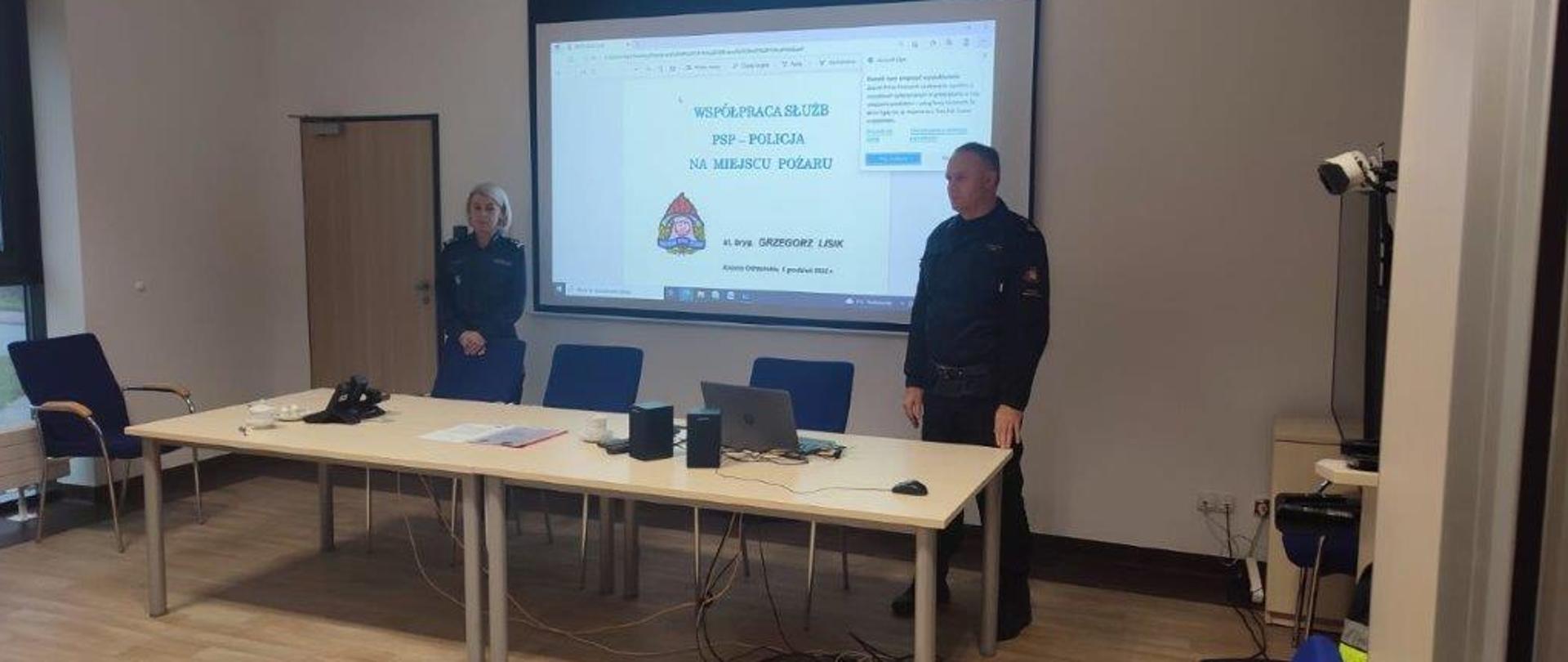 Zdjęcie przedstawia Zastępcę Komendanta Powiatowego Państwowej Straży Pożarnej w Krośnie Odrzańskim oraz Zastępcę Komendanta Powiatowego Policji młodszy inspektor Ewelina Bartkowiak na tle prezentacji z zakresu dochodzeń po pożarowych.