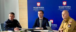 3 mężczyzn w tym wojewoda siedzą przy stole patrzą w kierunku wideokonferencji 