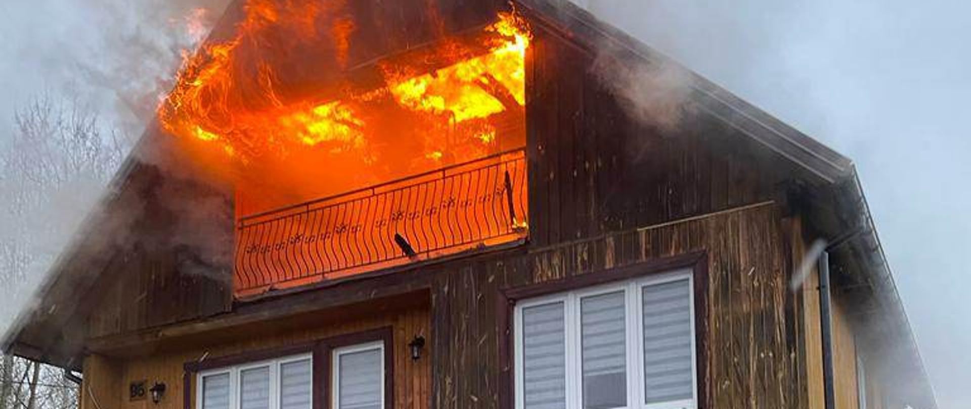 Pożar poddasza użytkowego w domu jednorodzinnym. Widoczny ogień wychodzący na zewnątrz. 