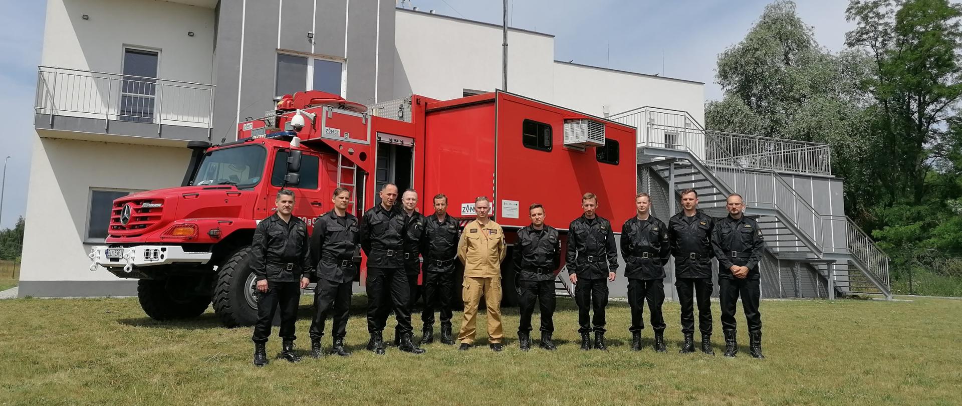 Zdjęcie pamiątkowe uczestników spotkania Zespołu ds. opracowania Zasad organizacji sztabu na potrzeby prowadzenia działań ratowniczych, na tle samochodu dowodzenia i łaczności