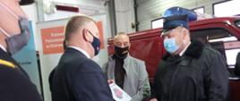 Na pierwszym planie senator Jarosław Rusiecki wręcza akt przekazania pojazdu prezesowi OSP Prawęcin. W tle garaż JRG Nr 1 w Ostrowcu Św.