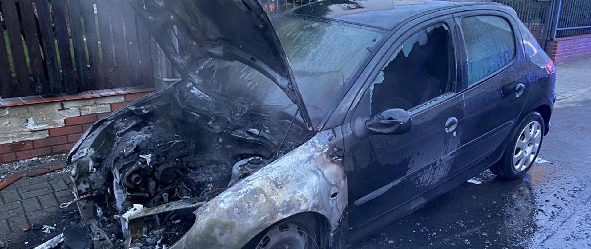 Spalony w przedniej części samochód stoi na ulicy Konstytucji.
