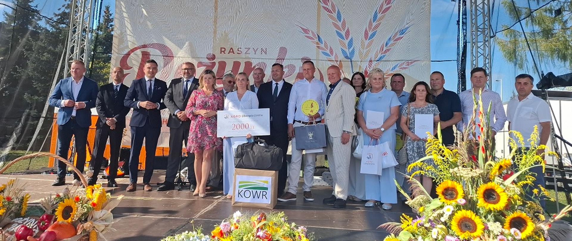 Na scenie plenerowej stoi około 25 osób. Są to organizatorzy oraz laureaci konkursu BGR. Laureaci Trzymają w rękach nagrody i dyplomy. 