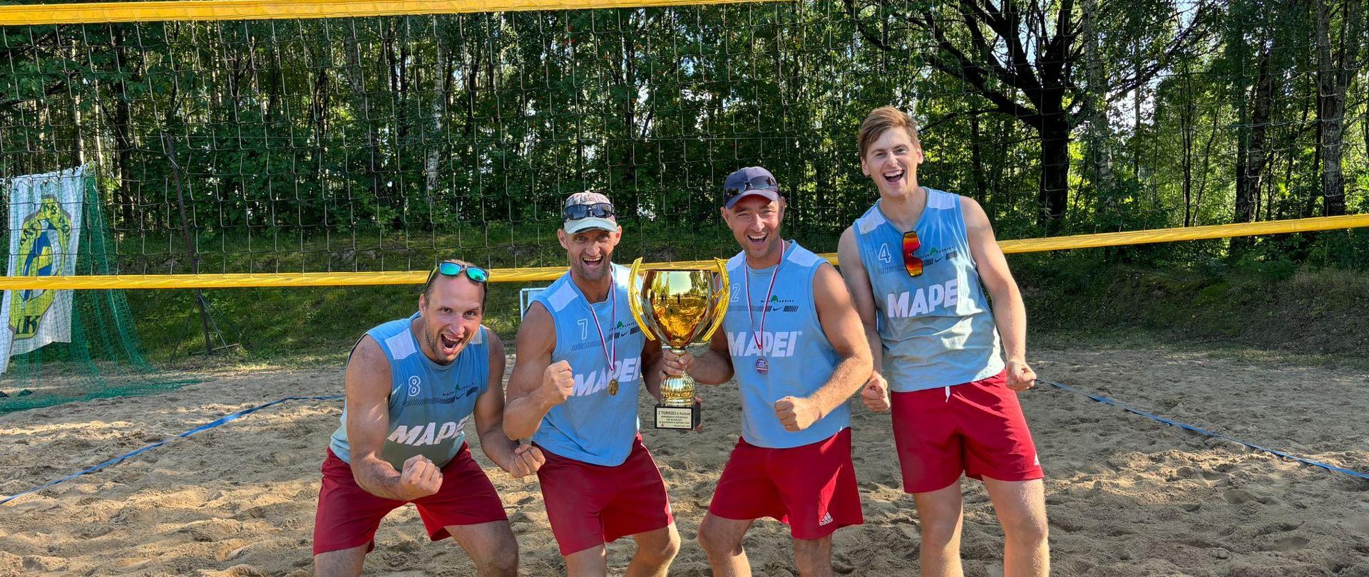 Dwie pary strażaków z Ełku na tle boiska do siatkówki plażowej