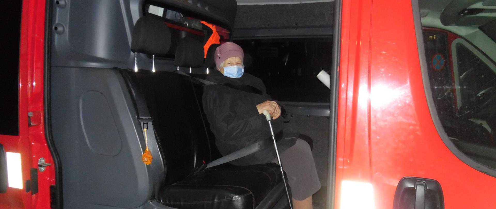 Kobieta w maseczce przeciwko covid-19 z laską siedzi w samochodzie strażackim typu furgon z przedziałem osobowym.